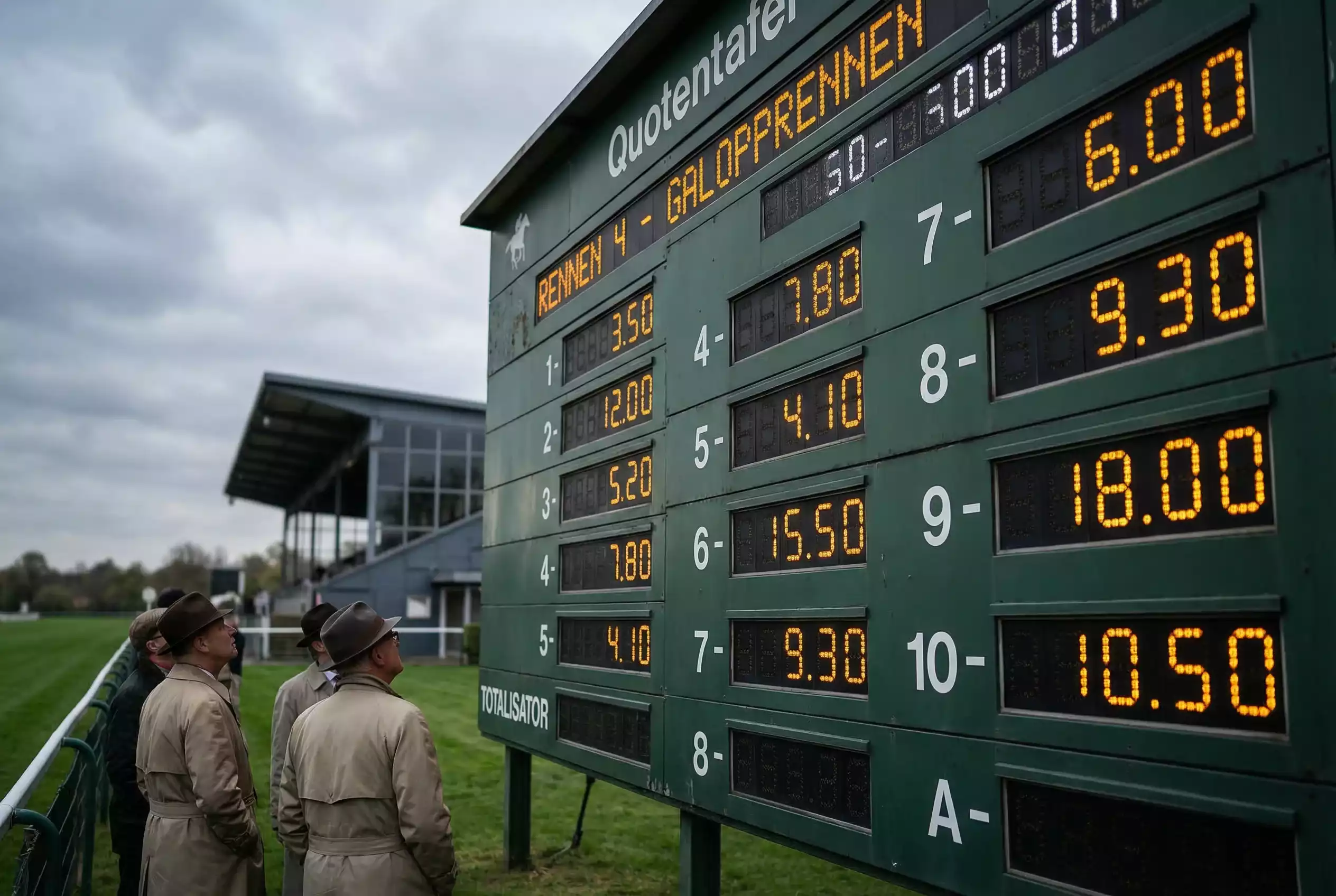 Pferdewetten Quoten verstehen – Quotentafel an einer Galopprennbahn mit Zuschauern im Hintergrund